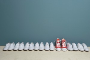 One pair of red shoes in a line of white shoes.